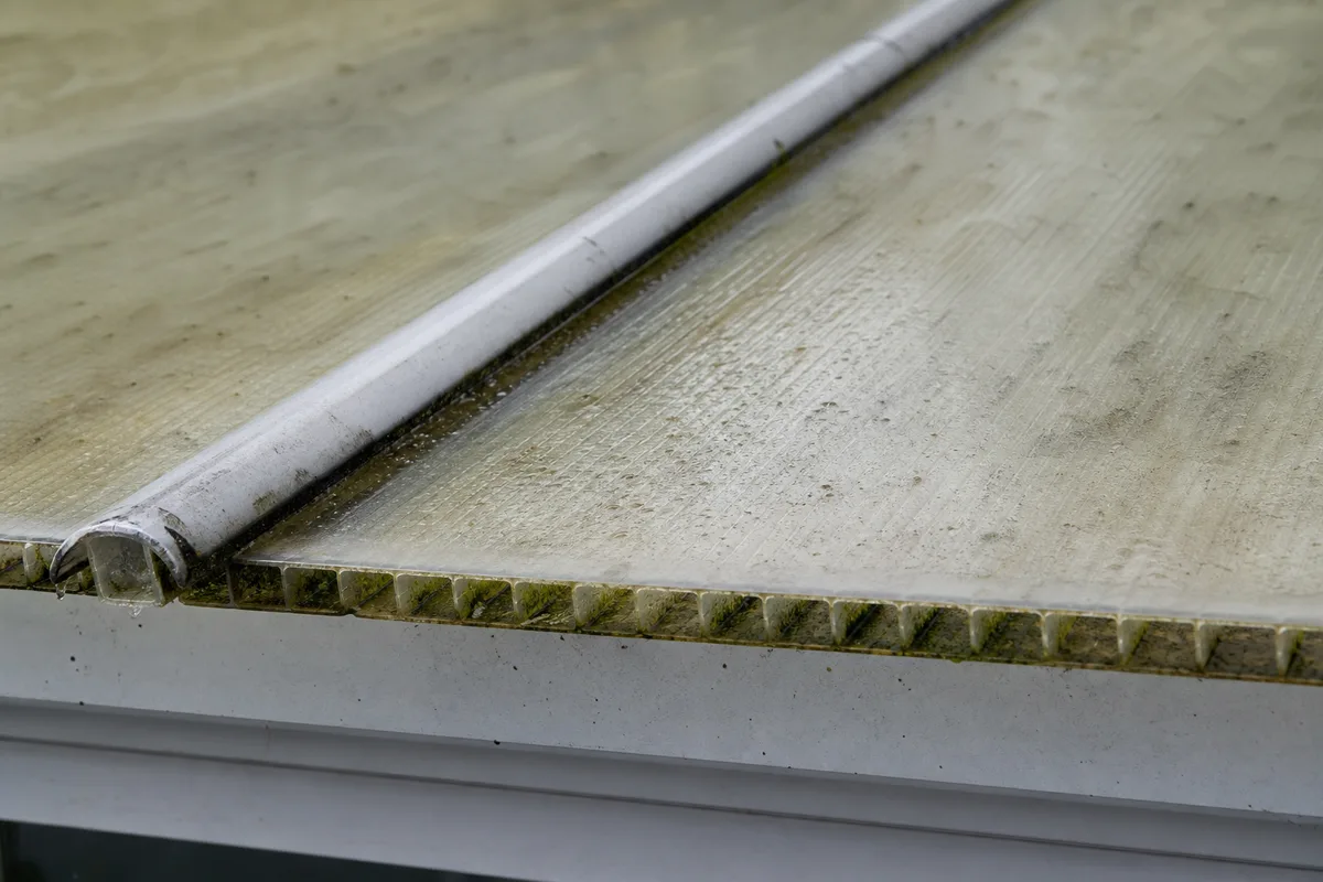 Toit de véranda en polycarbonate jauni avec traces de mousse, sous un ciel gris breton